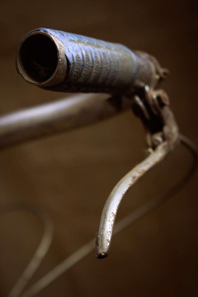 The handle bar of an old bicycle. The image has a narrow depth of filed with the end of the handle in sharp focus. The image is part of a series of photos of this bike, with each image concentrating on a different component.