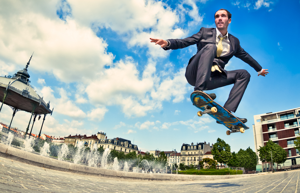 Man performing a skateboarding trick in a suit in a French town.  Commercial advertising style image.